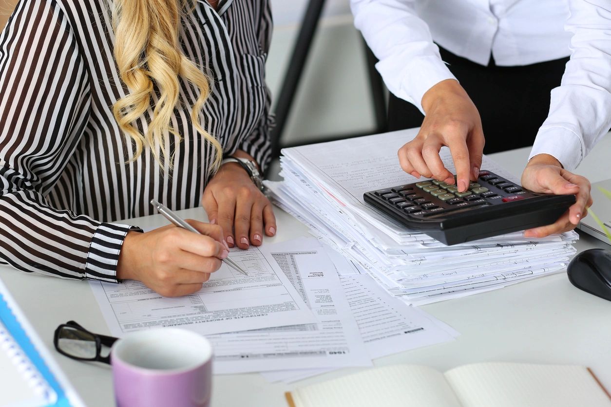 Two Female Accountants Counting on Calculator Income for Tax Form Completion Hands Closeup